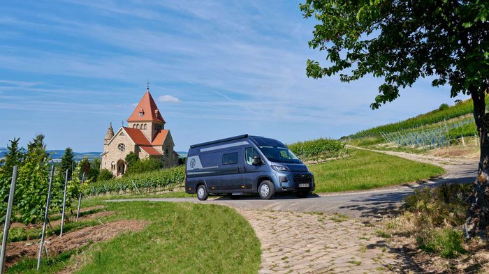 Karmann-Mobil Davis Lifestyle 620LS parkt vor einem Weinberg mit Kirche