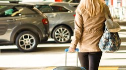 Eine Frau zieht einen Reisekoffer durch ein Parkhaus am Flughafen.  