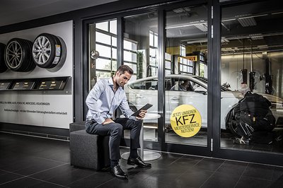 Ein Mann schaut auf sein Ipad und siezt in einem Auto Laden.