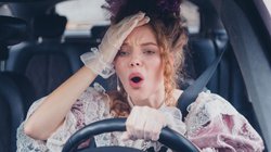 Frau mit Kostüm sitzt am Steuer und ist erschrocken. 