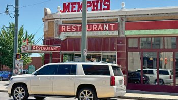 Weißes Auto fährt an typisch amerikanischem Diner mit Leuchtreklame vorbei.