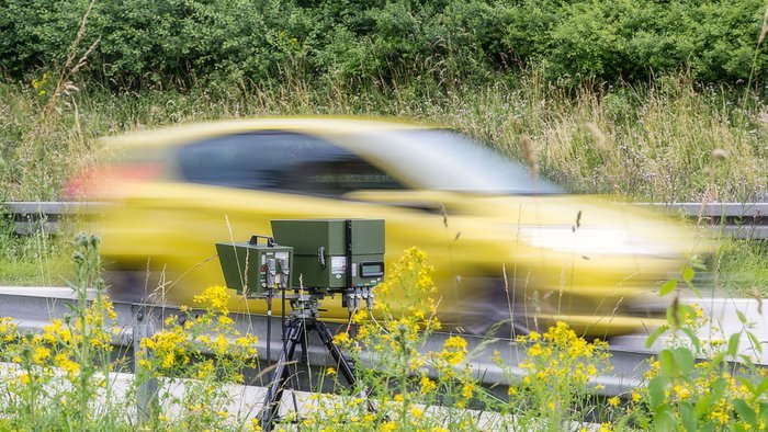 Ein gelbes Auto fährt in eine Geschwindigkeitskontrolle. 