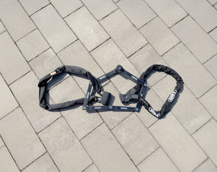 Ein Kettenschloss, ein Faltschloss und ein Fingerprint-Schloss liegen aufgereiht auf dem Boden.