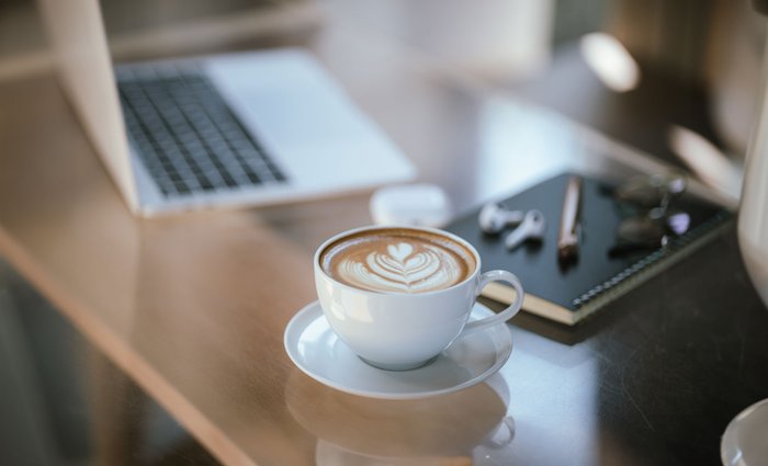 Eine Kaffeetasse steht auf einem Schreibtisch mit Laptop.
