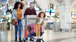 Eine Familie wartet am Flughafen-Terminal mit Gepäckwagen auf den Check-in.