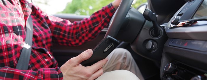 Ein Autofahrer hält ein Smartphone während einer Fahrt in der Hand.