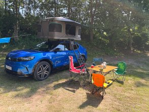 Vor dem Auto mit Dachzelt stehen ein Tisch und Stühle. 