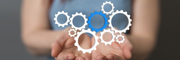 Mehrere ineinandergreifende Zahnräder schweben über zwei Händen.