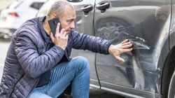 Mann begutachtet Schaden an seinem Auto. 