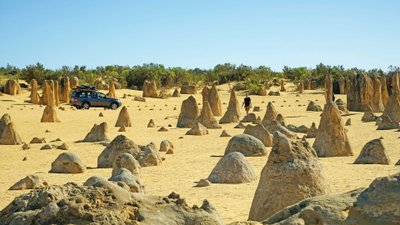 Landschaft, übersät mit Türmen aus Sandstein, dazwischen ein Auto und ein Wanderer.