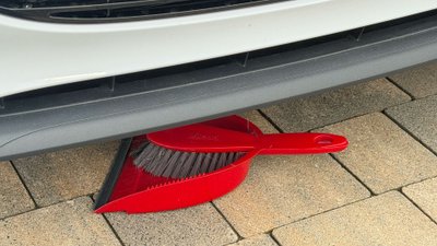 Kehrschaufel mit Besen unter einem Auto. 