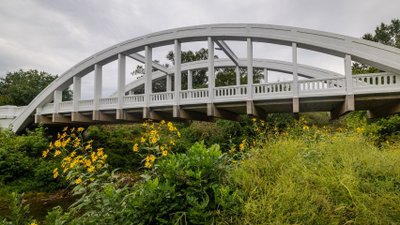 Blick auf weiße Bogenbrücke, die sich über einen Fluss spannt.