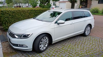 Weißes Auto parkt auf einem Parkplatz neben einem Busch.
