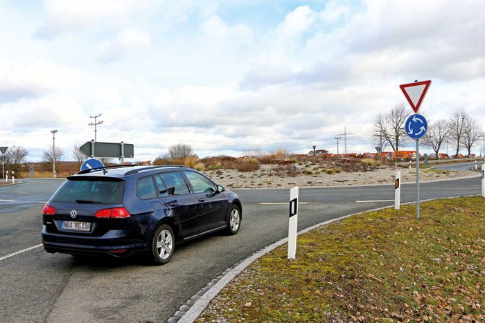 Ein Auto steht an einer Einfahrt zum beschilderten Kreisverkehr. 