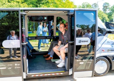 Personen sitzen im Roboterauto EDAG Citybot bei geöffneter Tür. 