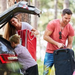 Eltern und zwei Kinder packen Gepäck in Kofferraum.