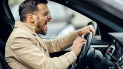 Wütender Mann sitzt im Auto und drückt auf die Hupe. 