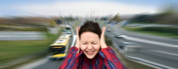 Frau hält sich die Ohren zu, im Hintergrund eine Straße mit Autos.
