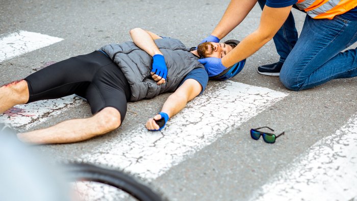 Ersthelfer versorgt verletzten Radfahrer nach Verkehrsunfall. 