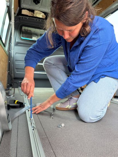 Eine Frau verschraubt Fixierschienen auf dem Boden eines Transporters. 