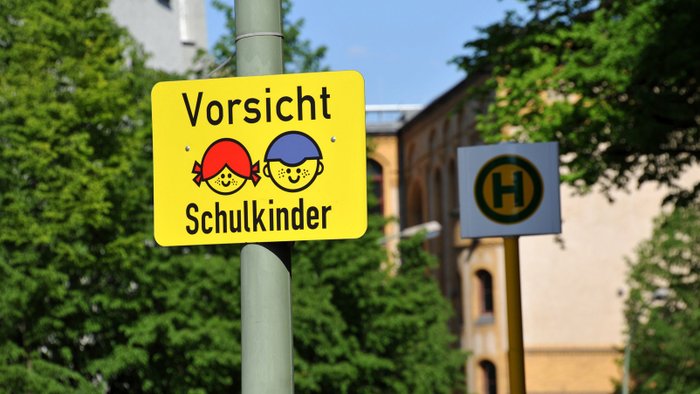 Kinder warten an der Straße, ein Auto biegt ab. 
