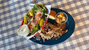 Teller mit Pulled Pork, Dip, Salat und Beilagen.