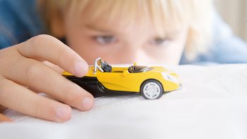 Kind schaut sich ein gelbes Spielzeugauto ganz genau an.