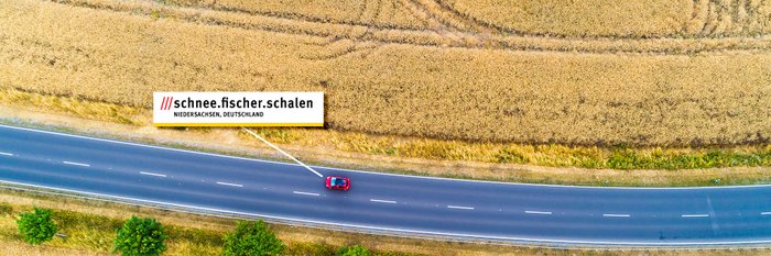 Ein Auto fährt auf einer Landstraße. Die 3-Wort-Adresse "schnee.fischer.schalen" steht in weißen Feld.