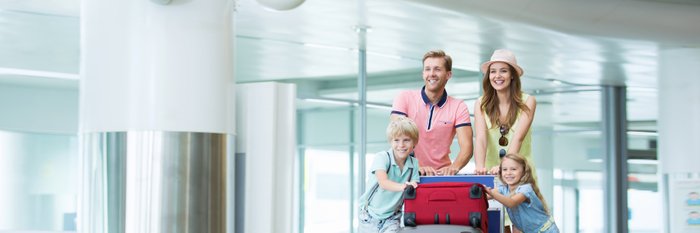 Junge Familie schiebt Gepäckwagen mit Koffern durch Flughafen.