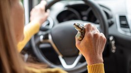 Ältere Frau raucht E-Zigarette beim Autofahren.
