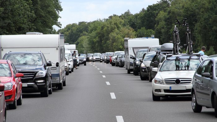 Autos und Wohnwagen stehen bei der Fahrt in den Urlaub auf einer Autobahn im Stau.