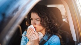Frau sitzt im Auto und putzt sich die Nase. 