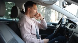Ein schläfriger Mann gähnt hinter dem Lenkrad eines Autos.