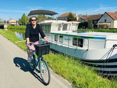 Frau fährt auf Fahrrad an einem Hausboot vorbei.
