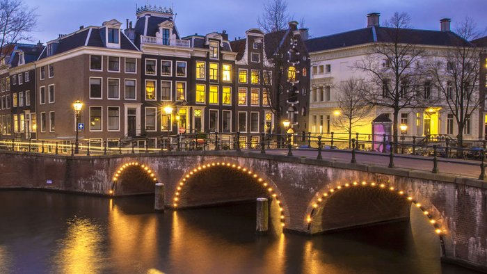 Blick auf einen Fluss in Amsterdam, im Hintergrund eine Brücke und Häuser.