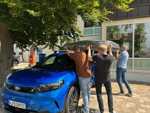 Vier Männer heben das Dachzelt auf das Autodach. 