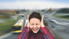 Frau hält sich die Ohren zu, im Hintergrund eine Straße mit Autos.