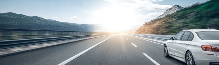 Auto fährt auf einer Autobahn bei tiefstehender Sonne.