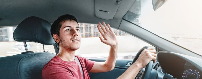 Ein Autofahrer grüßt freundlich nach draußen auf die Straße.
