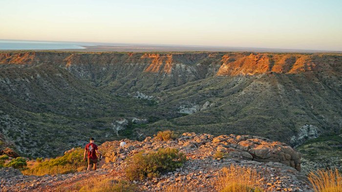 Zwei Wanderer laufen durch eine zerklüftete Tiefebene, dahinter das Meer.