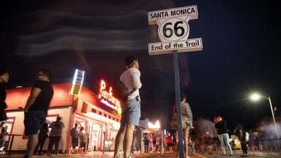 Blick auf den Santa Monika Pier bei Dunkelheit mit dem „End of the Trail“-Schild der Route 66 im Mittelpunkt.