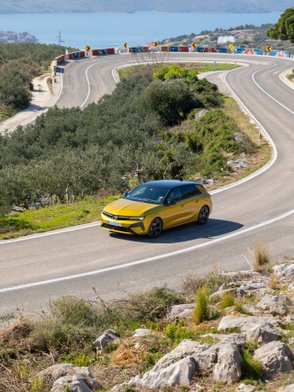 Ein gelber Opel Astra fährt auf einer kurvigen Straße. 