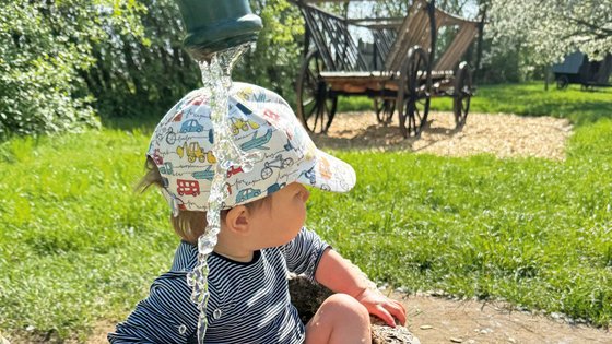 Ein Kind sitzt auf einer Wiese vor einem laufenden Brunnen.