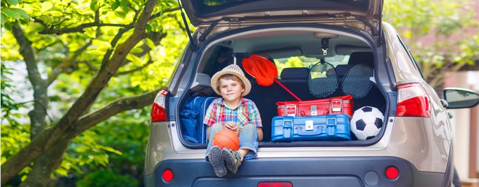 Ein kleiner Junge sitzt im Kofferraum eines Autos, das für den Urlaub mit Koffern beladen ist. 