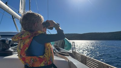 Ein Kind hält mit einem Fernglas auf einem Segelschiff in den Kornaten in Kroatien Ausschau.