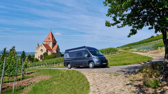 Karmann-Mobil Davis Lifestyle 620LS parkt vor einem Weinberg mit Kirche