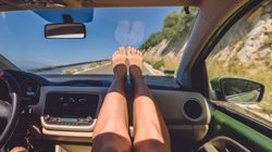 Frau hat die Füße auf das Armaturenbrett eines Autos gelegt. 