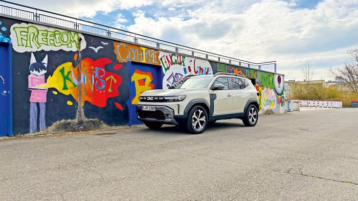 Dacia Duster Hybrid 140 parkt vor einer bunt bemalten Wand 