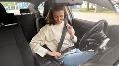 Eine junge Frau sitzt im Auto und schnallt sich an.  