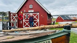 Rote Holzhäuser in skandinavischem Stil und ein Boot an einem Flussufer.